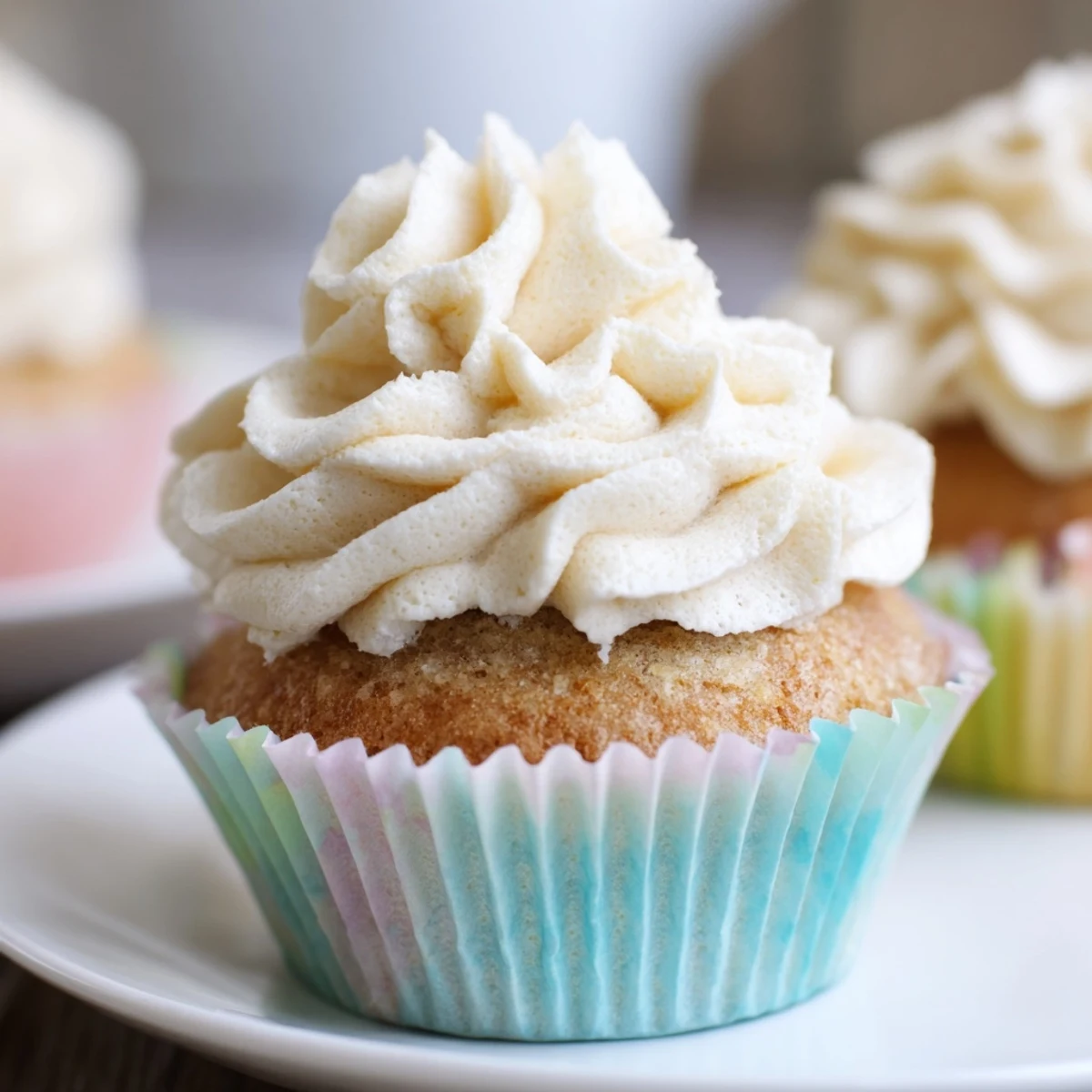 Fluffy vanilla cupcakes topped with swirling white buttercream frosting on a white plate