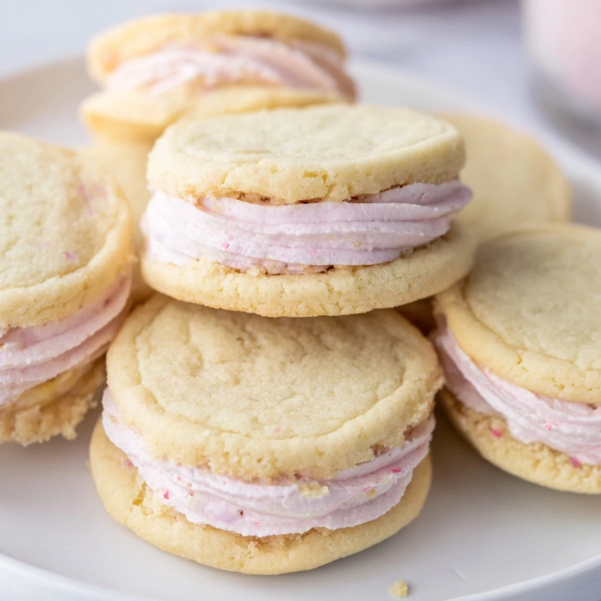 Delicate sugar cookie sandwiches with fluffy pastel buttercream peeking out from tender golden edges