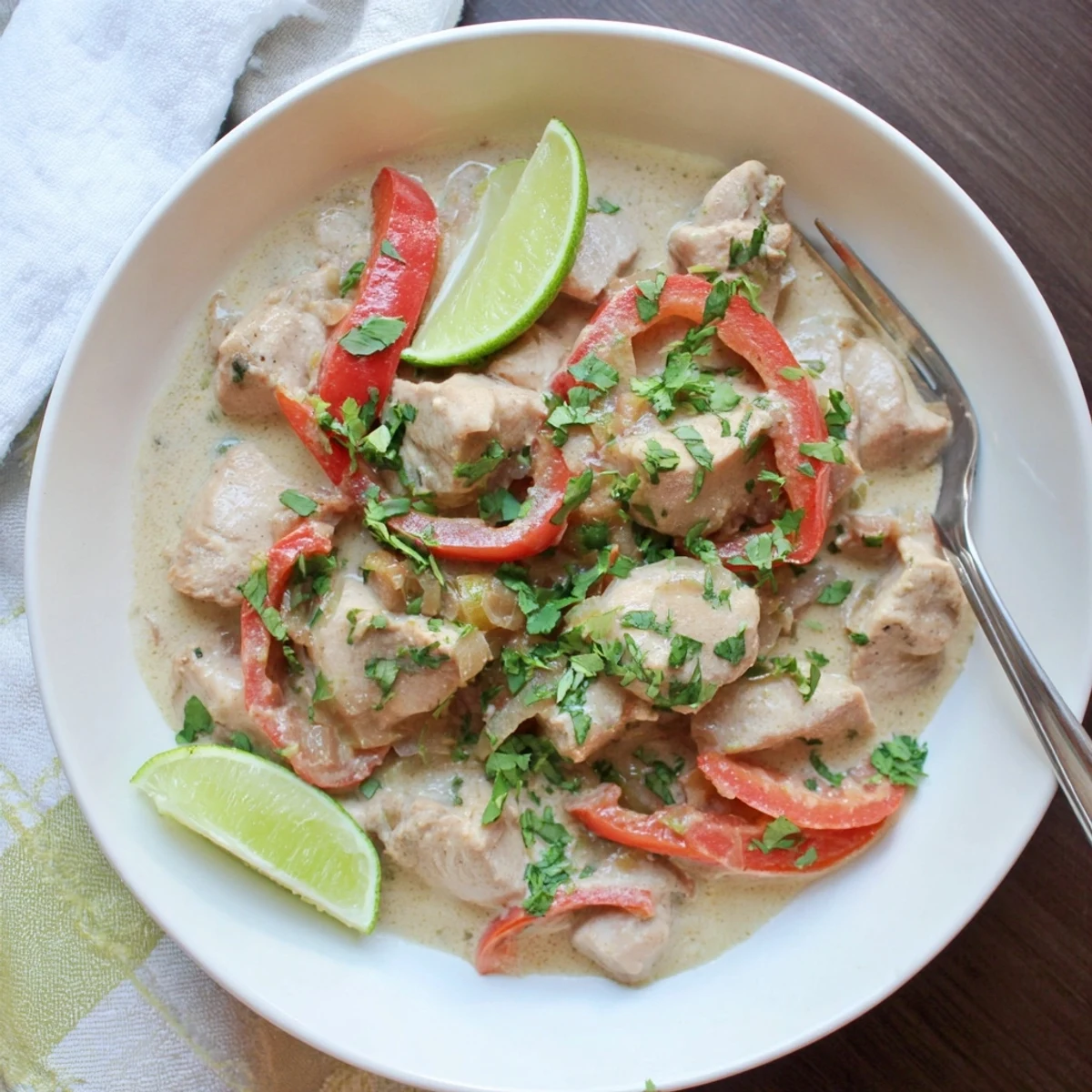 Tender Brazilian coconut chicken with colorful bell peppers and lime garnish on a rustic wooden table