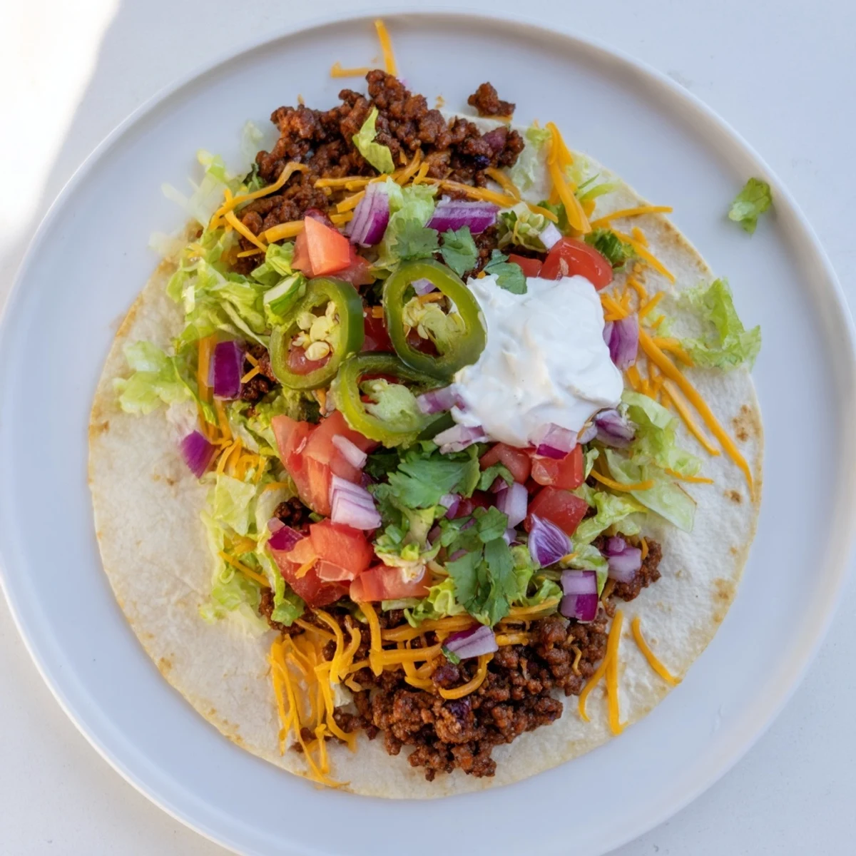 Golden crispy beef smash taco with melted cheddar and fresh colorful toppings on a griddle
