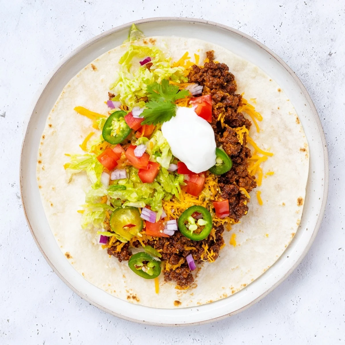 Juicy smashed beef patty taco bubbling with cheese served with lettuce tomatoes and sour cream