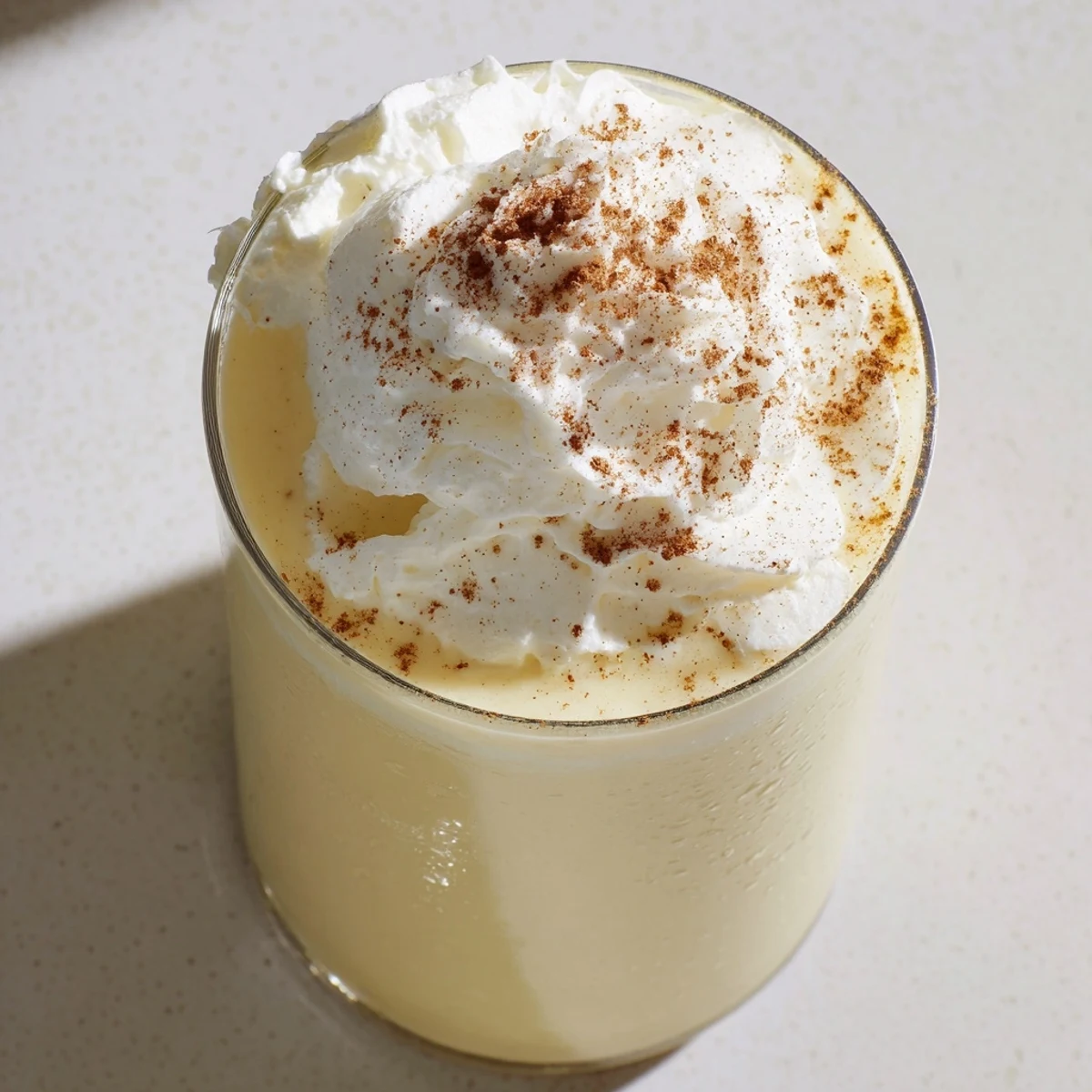 Golden keto eggnog topped with fluffy whipped cream and dusted with nutmeg