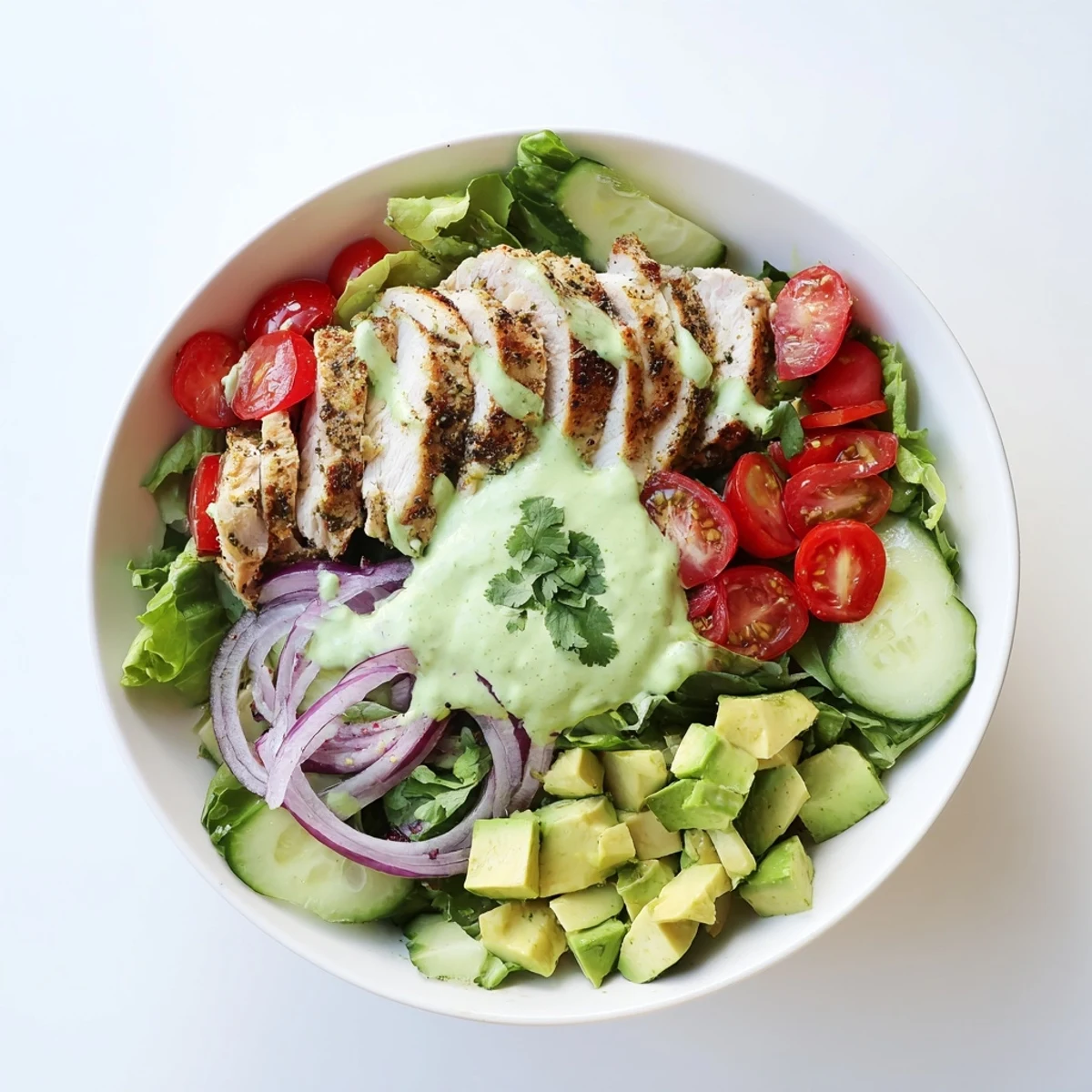 Creamy avocado grilled chicken salad bowl with juicy sliced chicken, fresh vegetables, and tangy green dressing drizzled over mixed greens