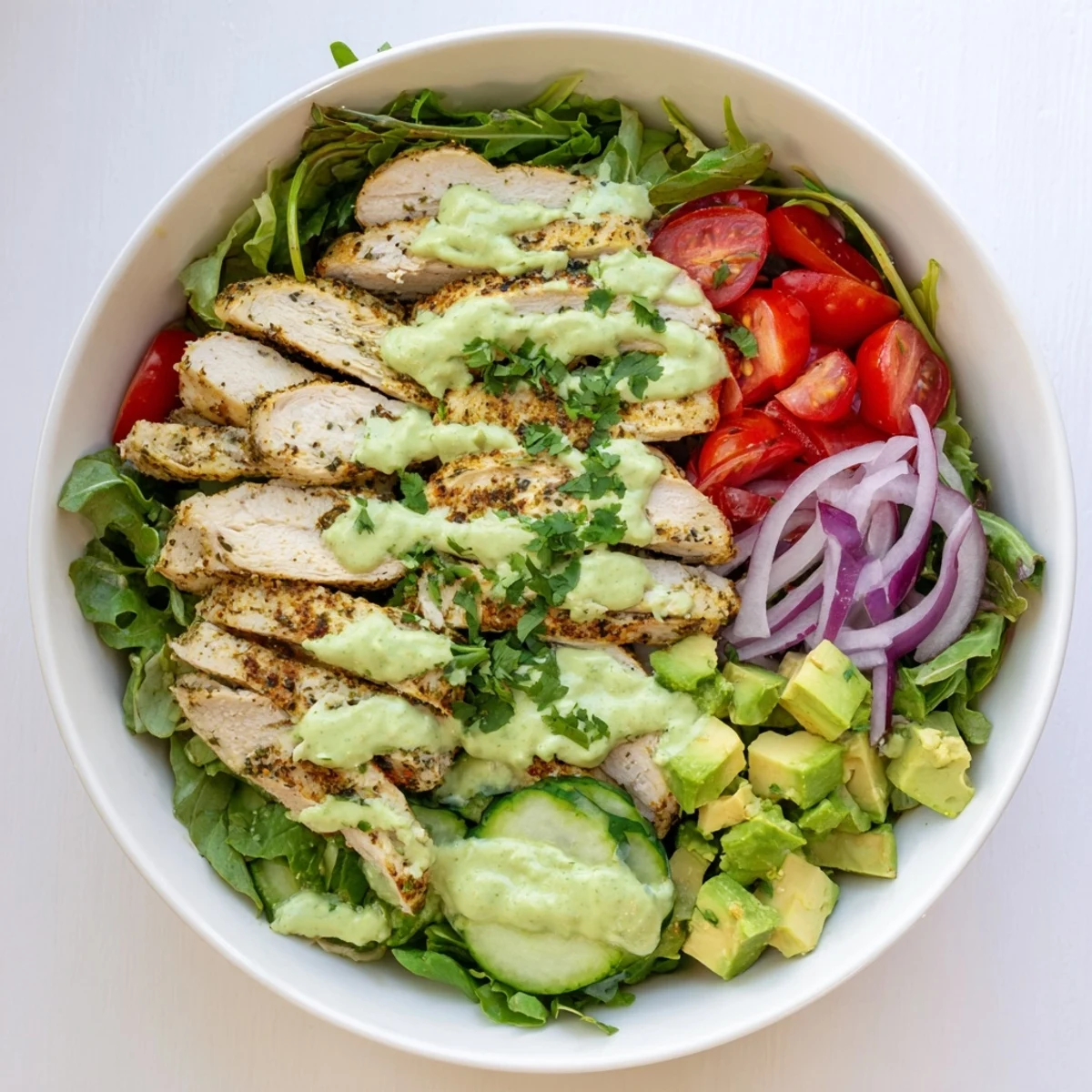 Nutritious grilled chicken salad bowl topped with creamy avocado dressing, fresh salad greens, vegetables, and sliced grilled chicken breast