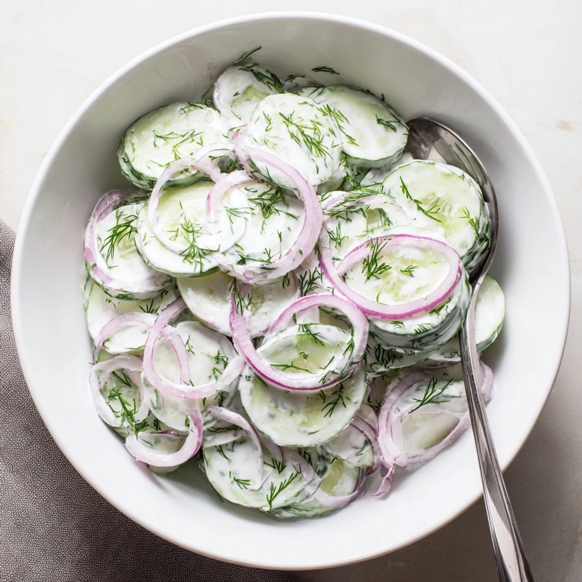 Bowl of crisp cucumber dill salad topped with fresh herbs and red onion