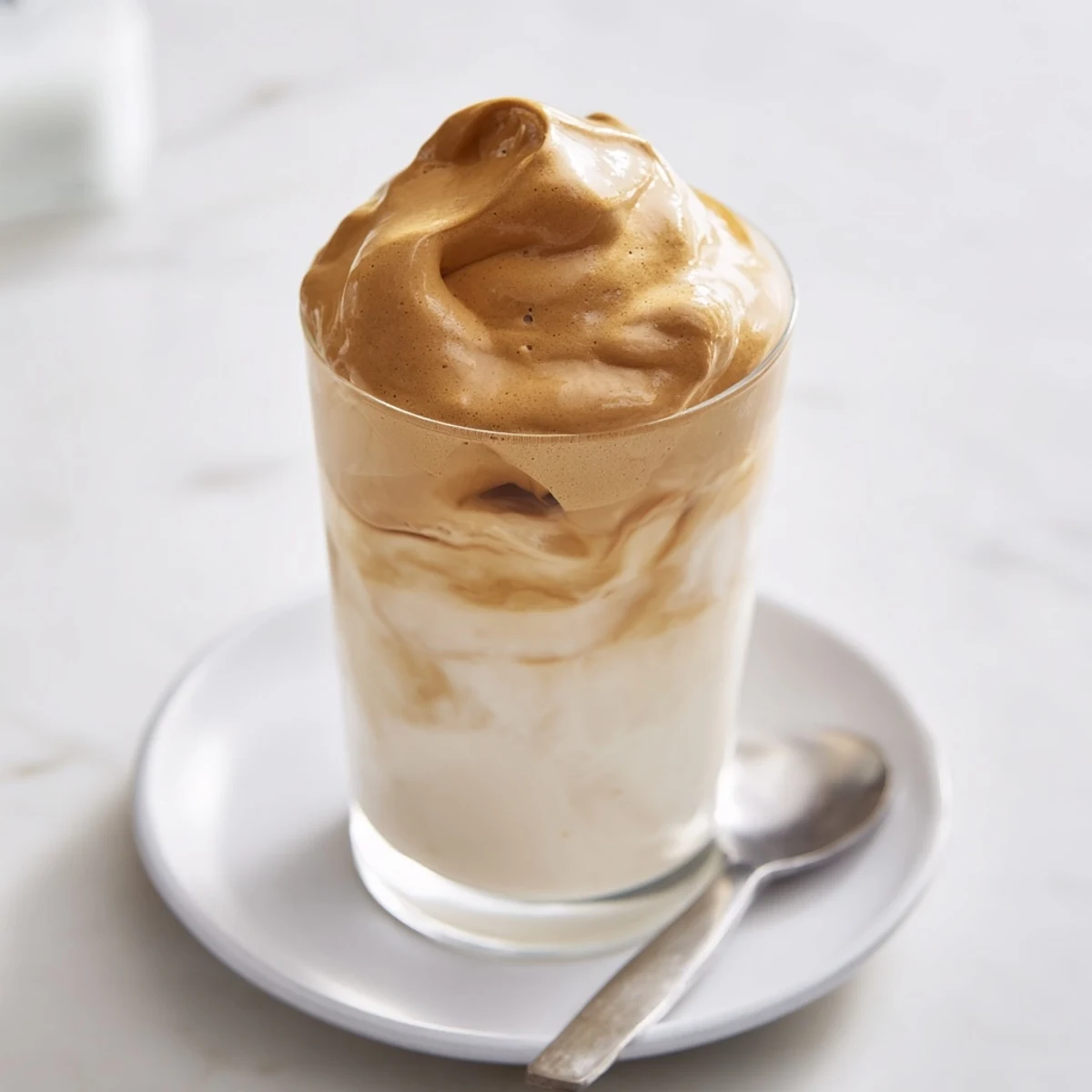 Whipped Coffee dollop atop iced milk, airy texture and creamy marbling