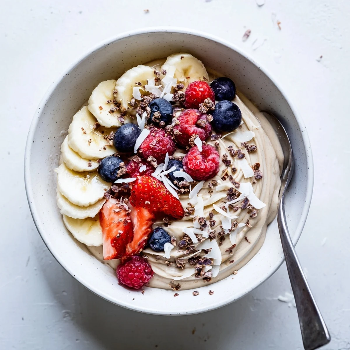 Smooth and swirlable healthy nice cream recipe scooped into a glass with chopped nuts and fresh fruit garnish