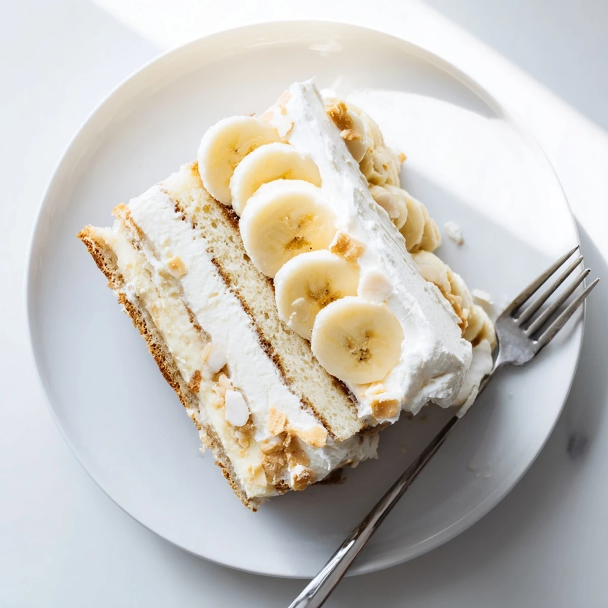 Golden slice of banana pudding cake revealing layered vanilla custard and fresh banana slices between moist cake rounds