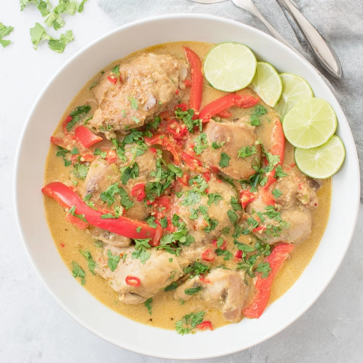 Golden chicken pieces swimming in rich, creamy coconut sauce with vibrant red peppers and fresh cilantro garnish.