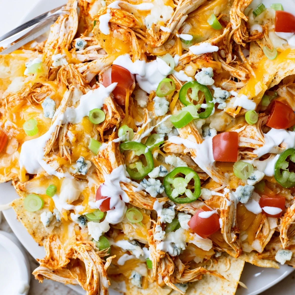 Game-day Buffalo Chicken Nachos topped with diced tomatoes, green onions, blue cheese