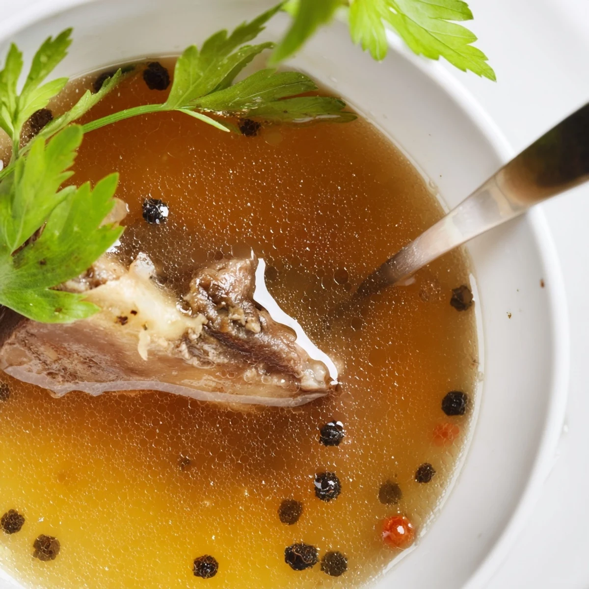 Warm mug of Beef Bone Broth steaming, golden liquid with herb flecks