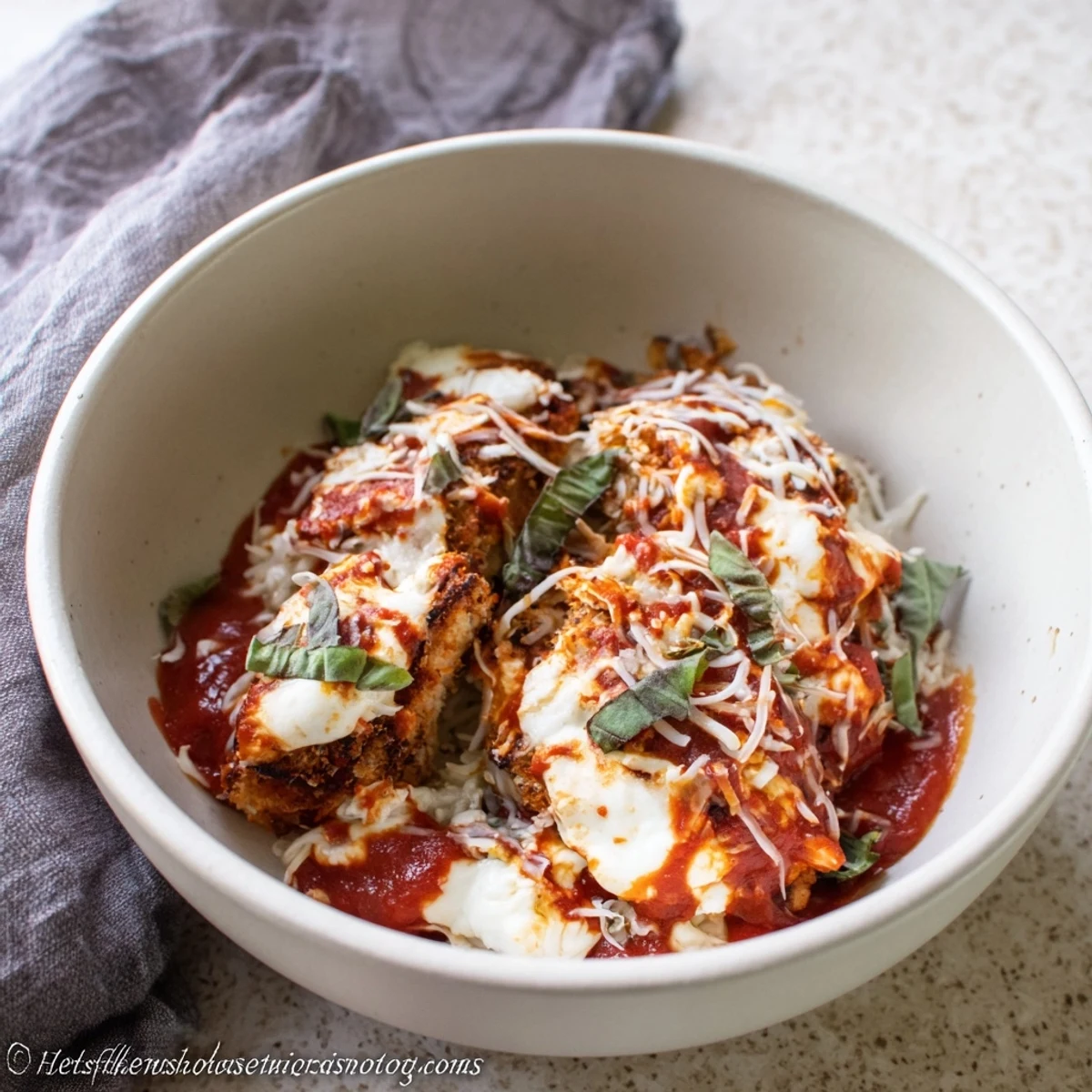 Golden baked chicken parmesan layered over creamy cottage cheese in a bowl with melted mozzarella and fresh basil garnish