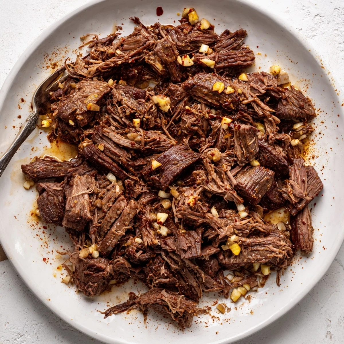 Golden shredded slow cooker beef barbacoa steaming in a serving dish with lime wedges