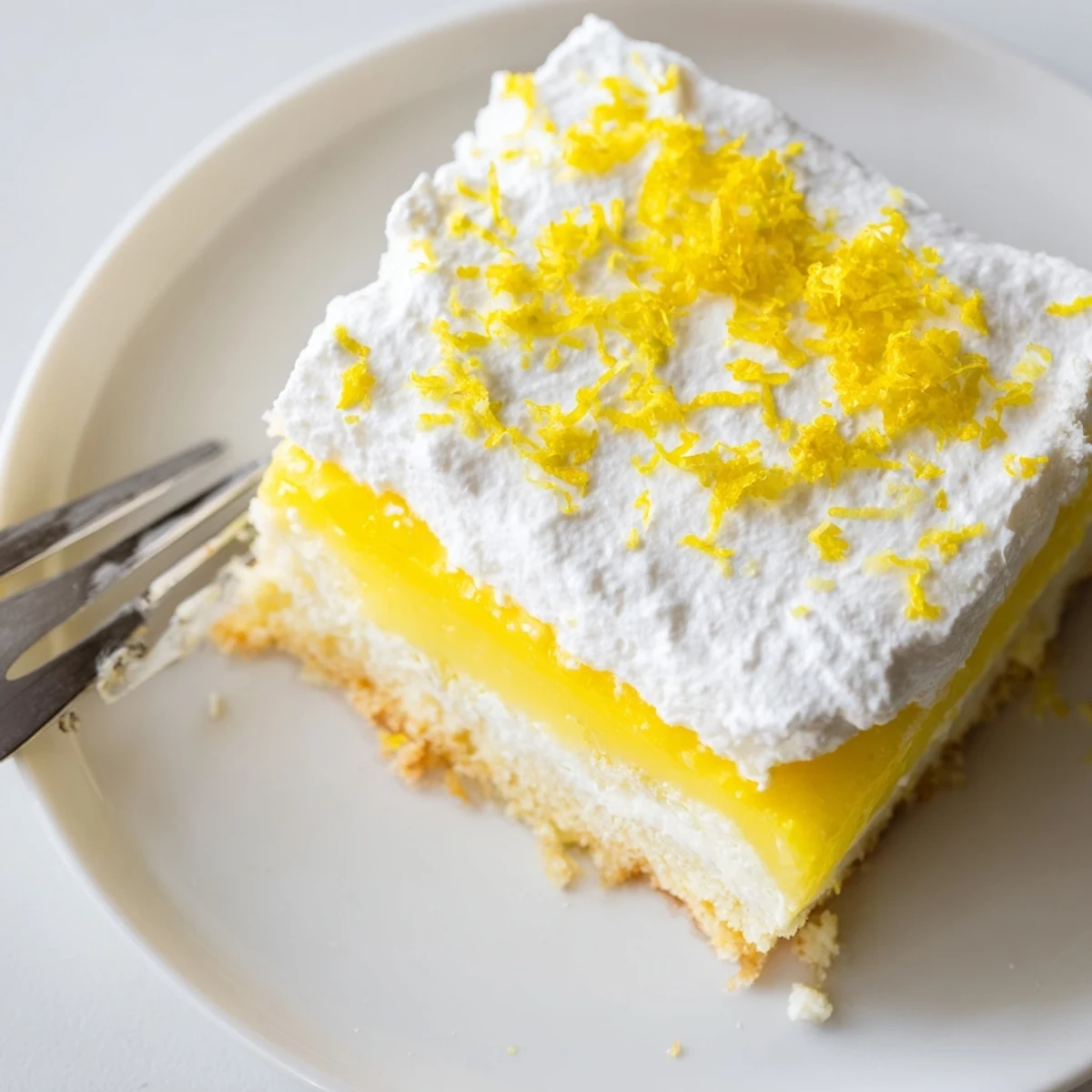 Layered lemon lush cake dessert with buttery crust, creamy filling, and fluffy whipped topping garnished with bright zest