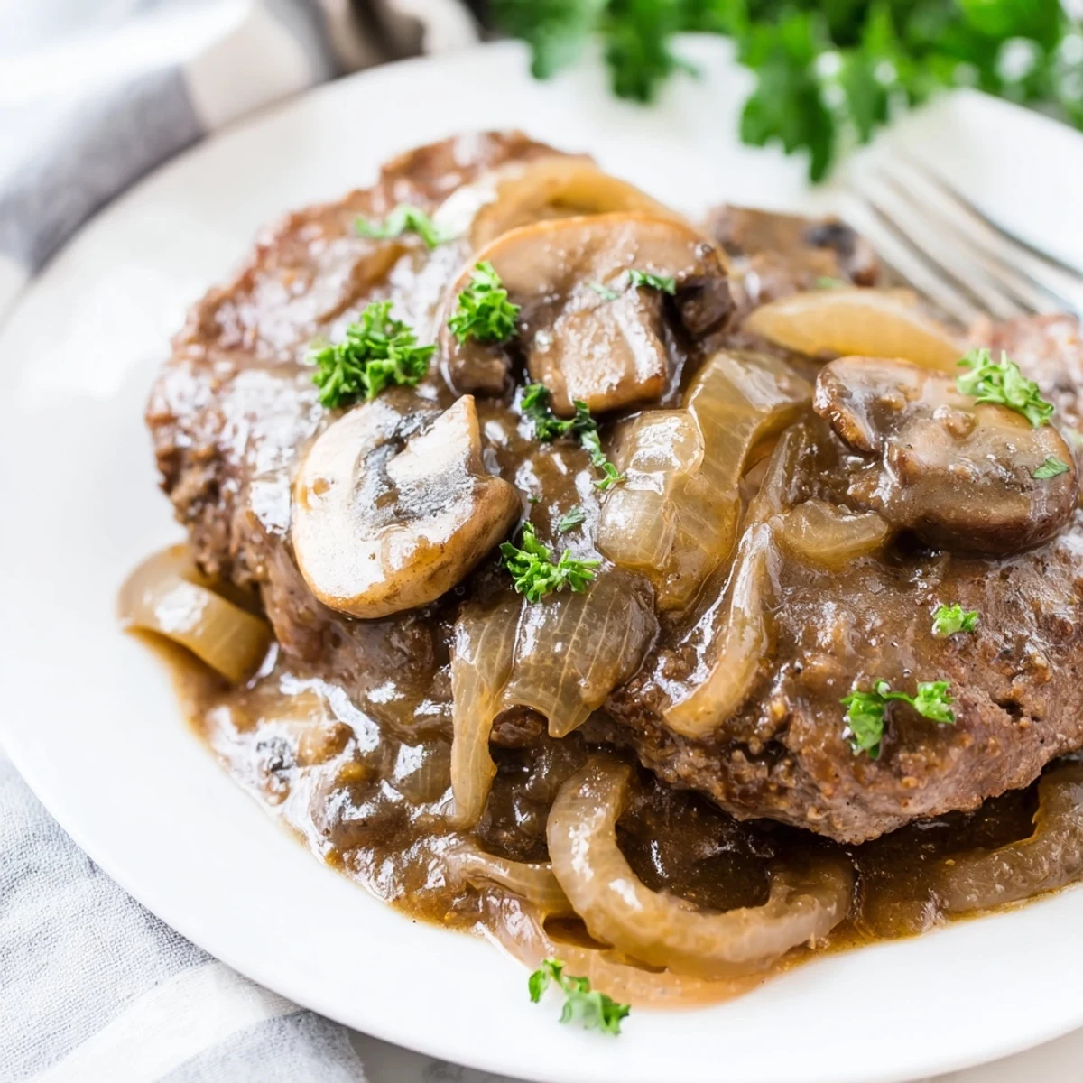Golden brown cube steaks simmering in rich onion mushroom gravy with fresh parsley garnish