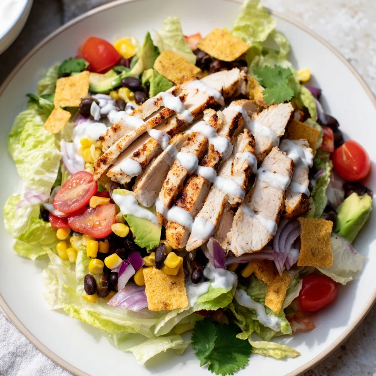 Colorful Southwestern chicken salad bowl topped with grilled sliced chicken breast, avocado, black beans, corn, tomatoes and zesty lime yogurt dressing over crisp romaine lettuce