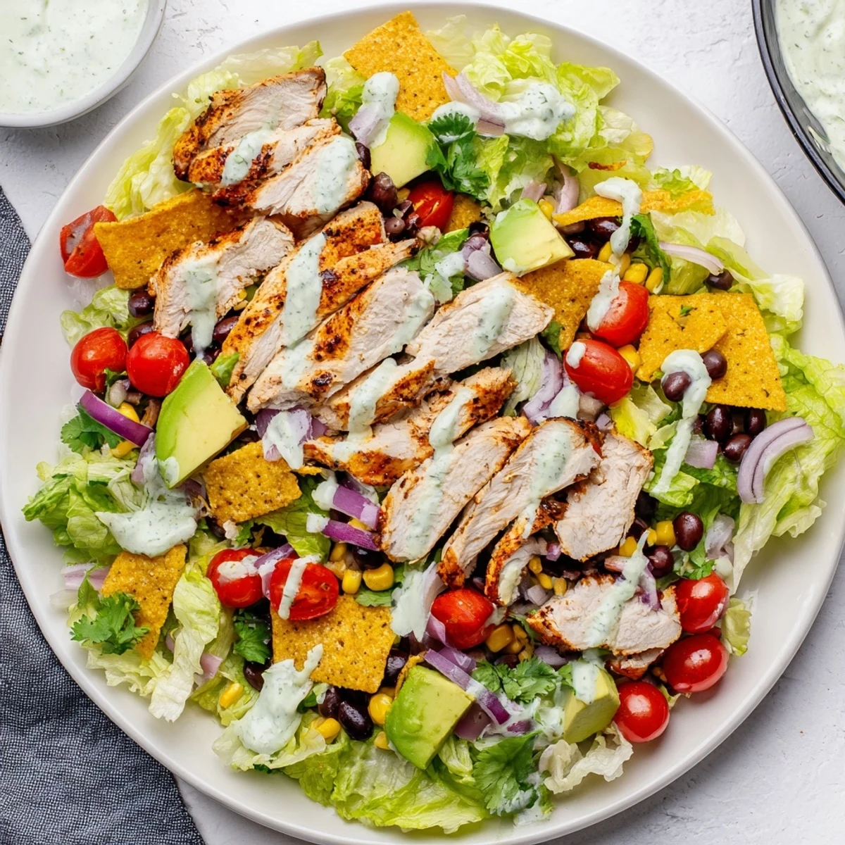 Fresh Southwestern chicken salad featuring spiced grilled chicken strips, crisp vegetables, creamy dressing and tortilla strips garnish arranged in a vibrant layered serving bowl