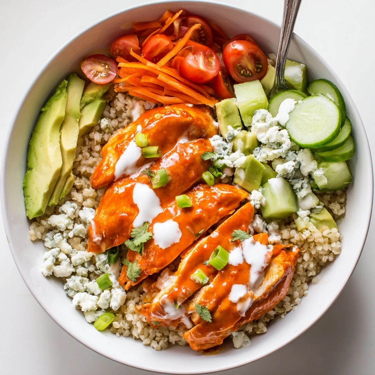 Buffalo chicken grain bowl topped with diced avocado crumbled blue cheese and fresh herbs