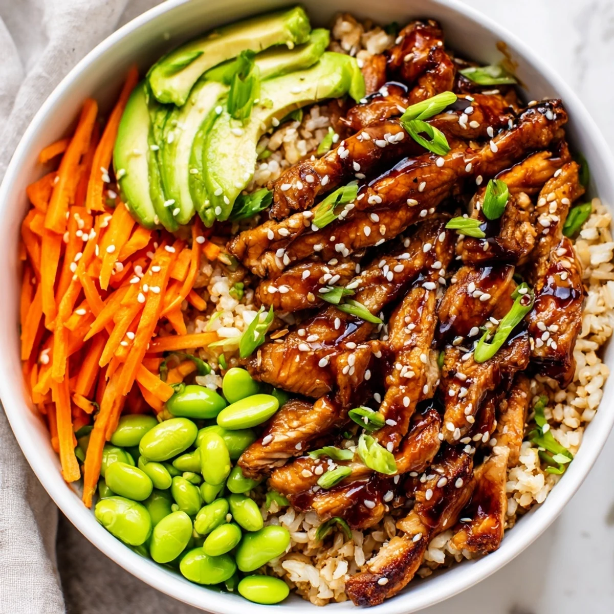 Steaming teriyaki chicken grain bowl with sliced avocado and vibrant fresh greens