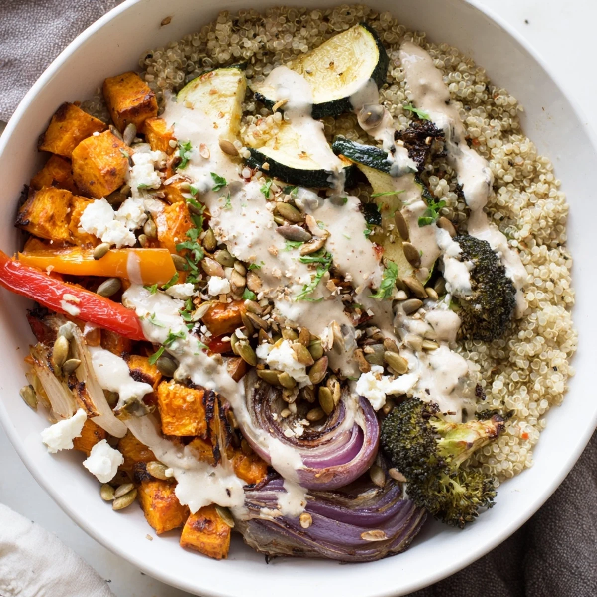 Golden roasted vegetables piled on fluffy quinoa in a vibrant grain bowl with tahini drizzle.
