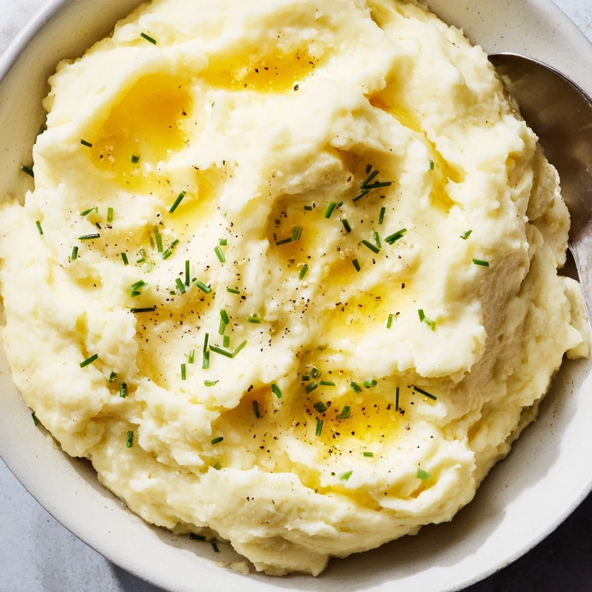 Steaming bowl of velvety mashed potatoes garnished with fresh chives and cracked pepper