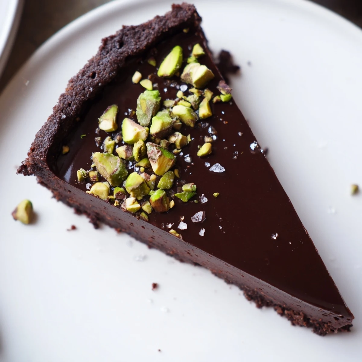 Dark Chocolate Pistachio Tart sliced on a rustic board with crumbly chocolate crust