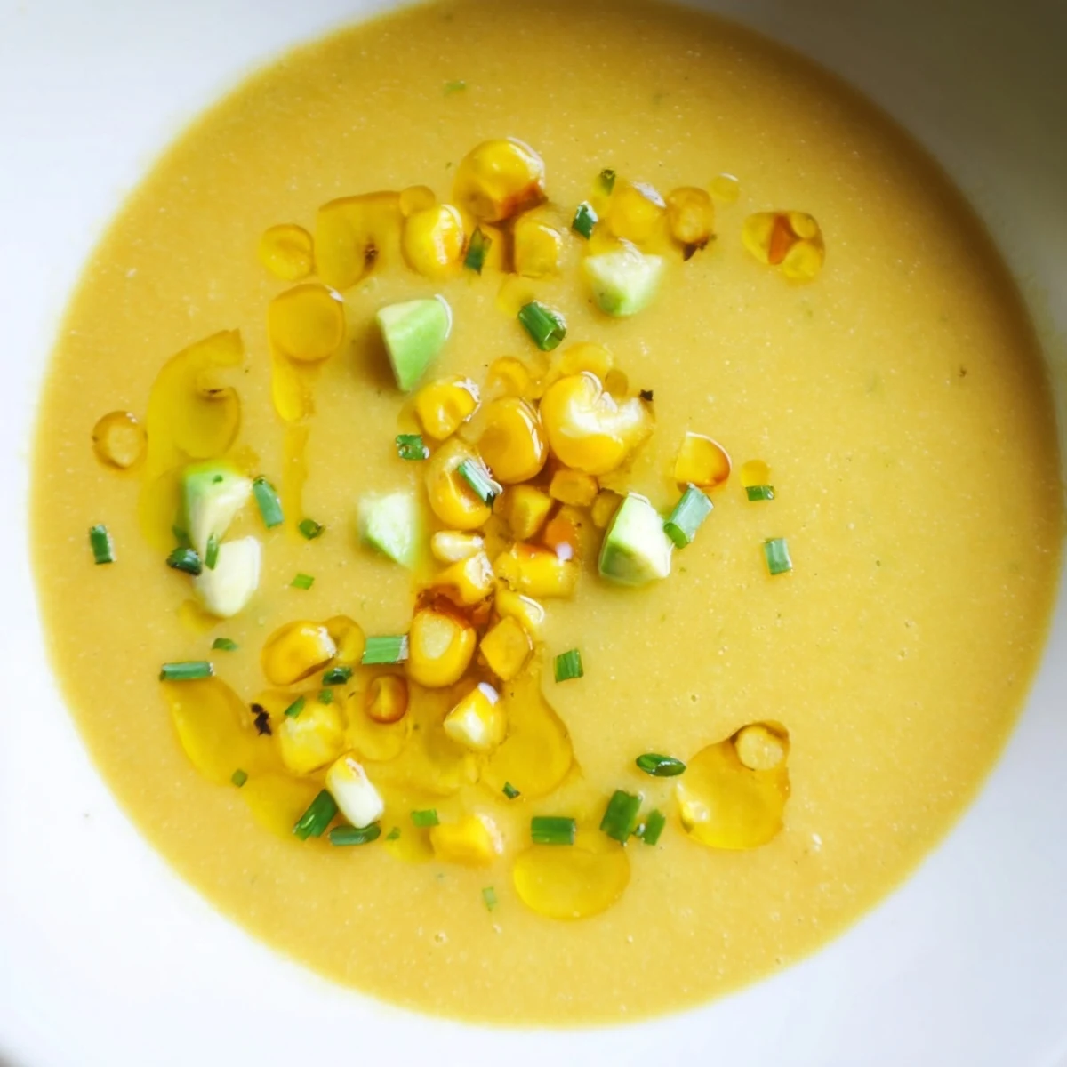 Vibrant yellow summer sweet corn gazpacho drizzled with olive oil in a rustic bowl