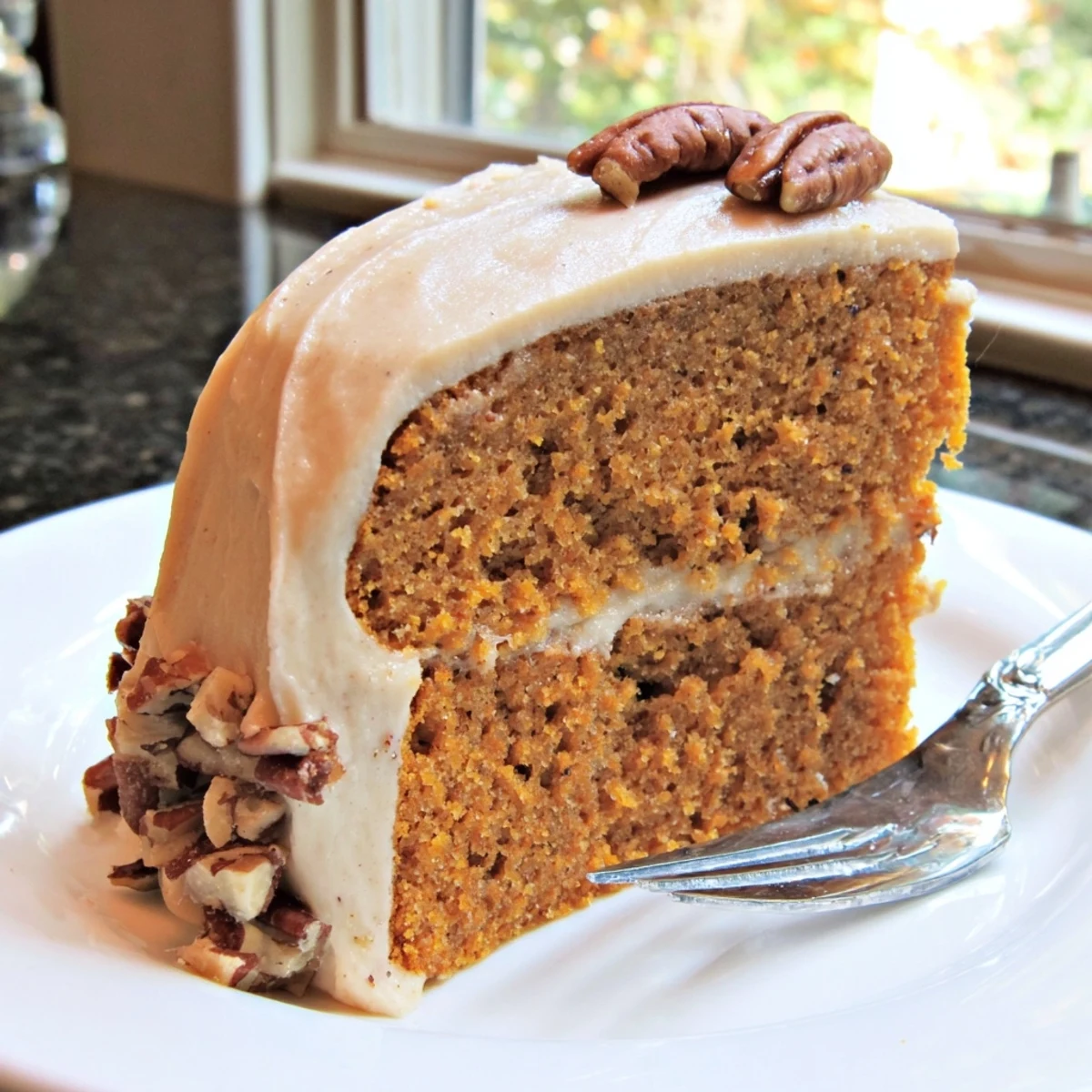 Moist pumpkin pecan cake topped with swirled cinnamon cream cheese icing and scattered toasted pecan pieces