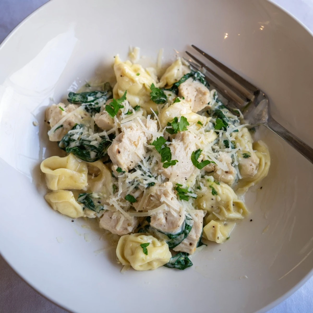 Tender seared chicken and cheese tortellini tossed in creamy garlic spinach sauce on a white plate