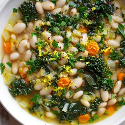Healthy White Bean and Kale Soup with Lemon Zest ladled from a large pot, filled with hearty vegetables and a bright citrus zest finish.