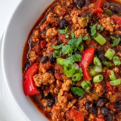 Homemade Turkey Chili with Black Beans and Tomatoes served in a rustic bowl topped with avocado and cilantro.