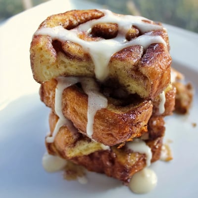 Warm, custardy Cinnamon Roll French Toast Bites piled on a breakfast plate with maple syrup and powdered sugar.