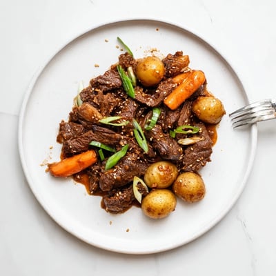 Fork-tender Slow Cooker Korean Beef Pot Roast With Soy Garlic Gravy served with carrots and potatoes on a platter.