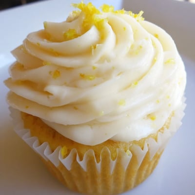 A close-up of a Limoncello Cupcake with fluffy frosting, fresh lemon zest garnish, and a delicate crumb showing in a soft kitchen light.  